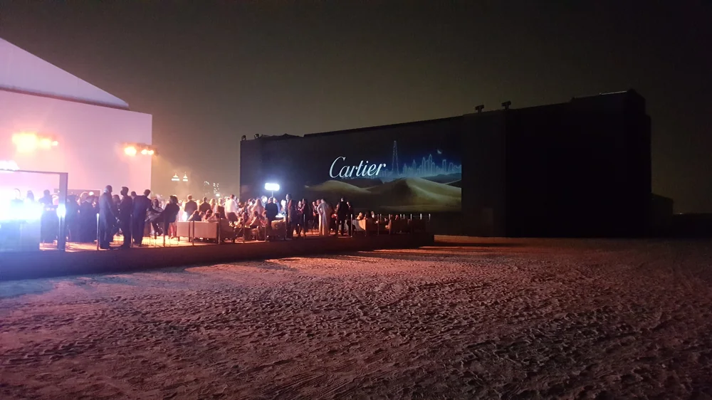 Les invités rassemblés dans le désert devant la projection du film Cartier Mirage sur écran géant.