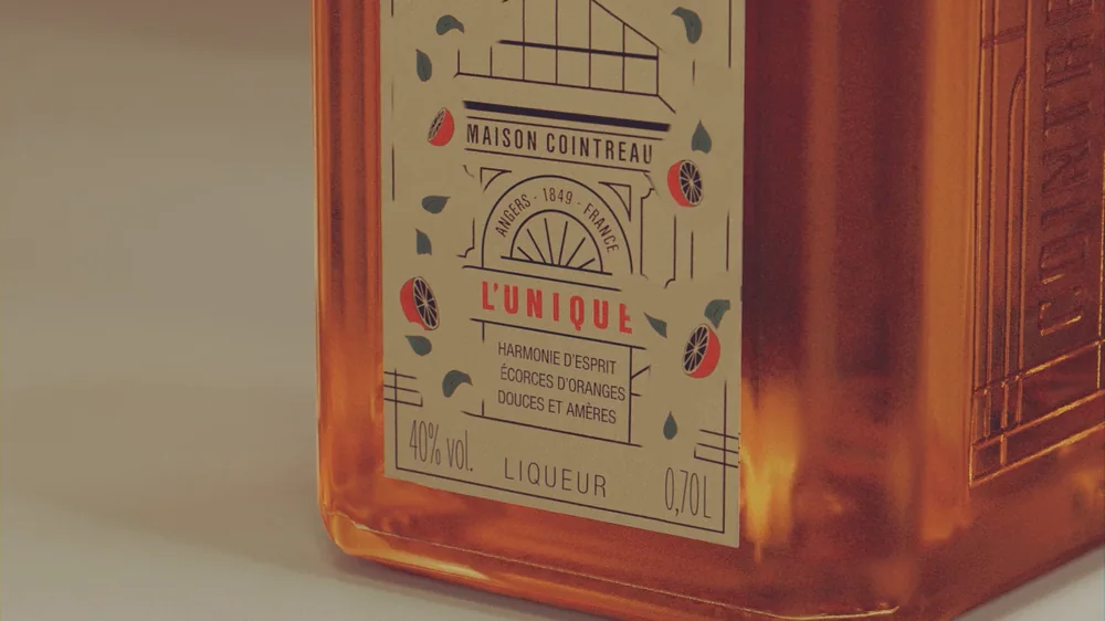 Angle du flacon Cointreau en 3D, étiquette « L'Unique », grain et reliefs du papier restitués en gros plan.