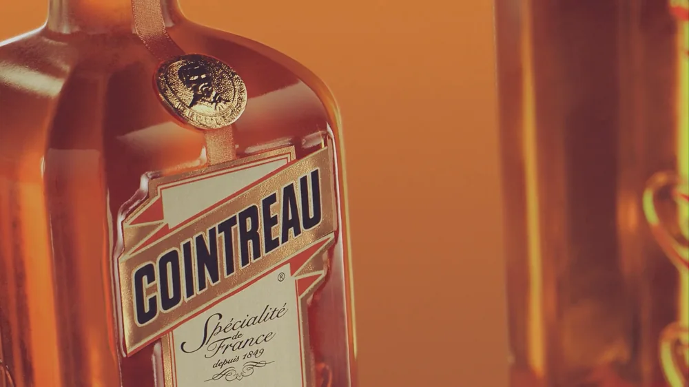 Détail du flacon Cointreau en 3D : étiquette en ruban, capsule métallique gravée et reflets sur le verre ambré.