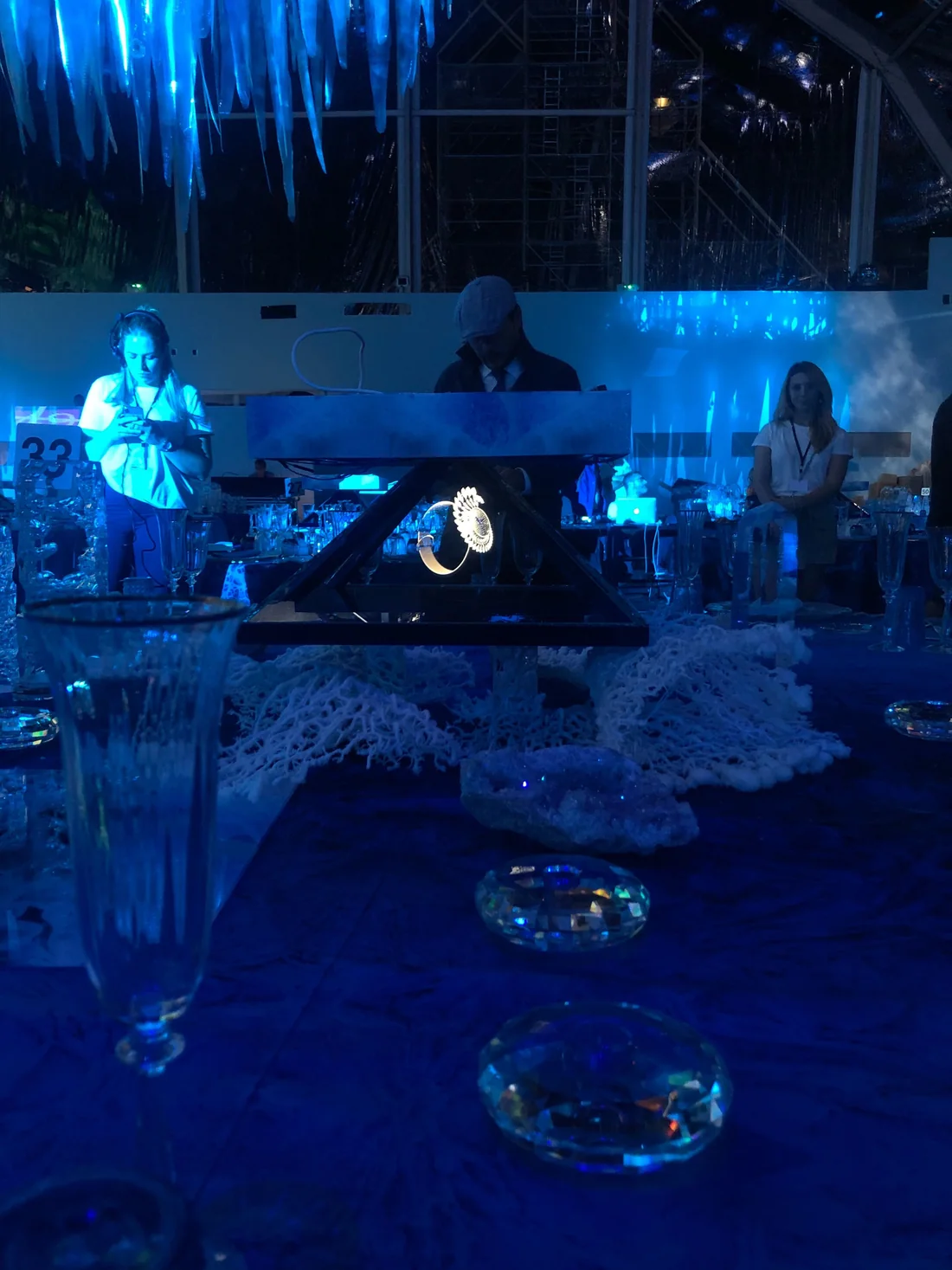 Bijou en hologramme apparaissant au centre d'une table, à côté de verres à champagne, pendant la vente aux enchères.