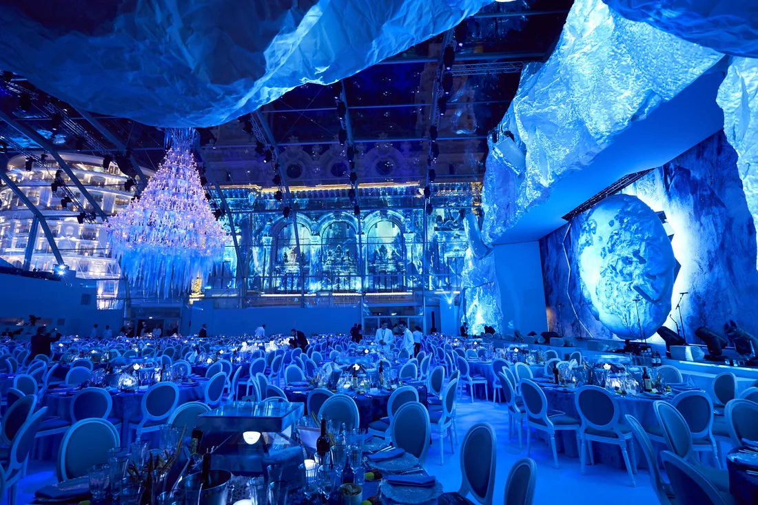 Salle du Gala des Océans, décor de banquise et sculptures de glace éclairées en bleu, tables dressées.