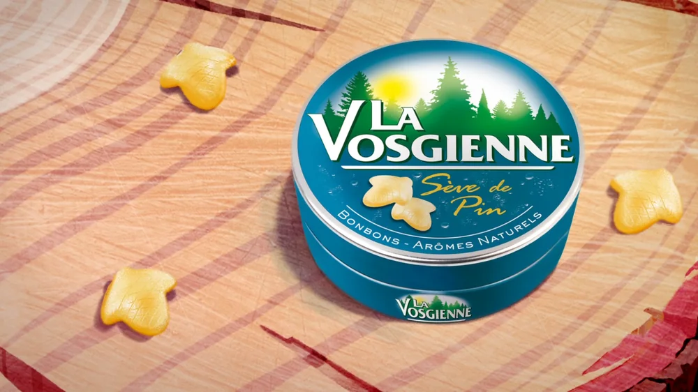 Billboard TV La Vosgienne : la boîte de bonbons à la sève de pin posée sur un plan de bois, bonbons disposés autour.