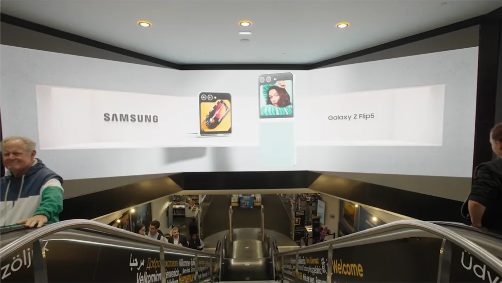 Le même dispositif avec un contenu anamorphique : les téléphones semblent sortir de l'écran et flotter au-dessus des escalators.